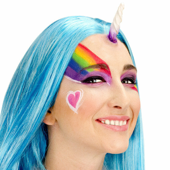 Person with blue hair and unicorn horn, wearing colorful makeup and a heart sticker.