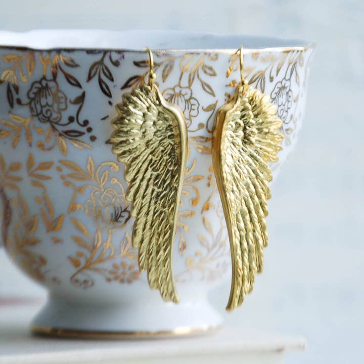 Golden Wing earrings hanging from cup