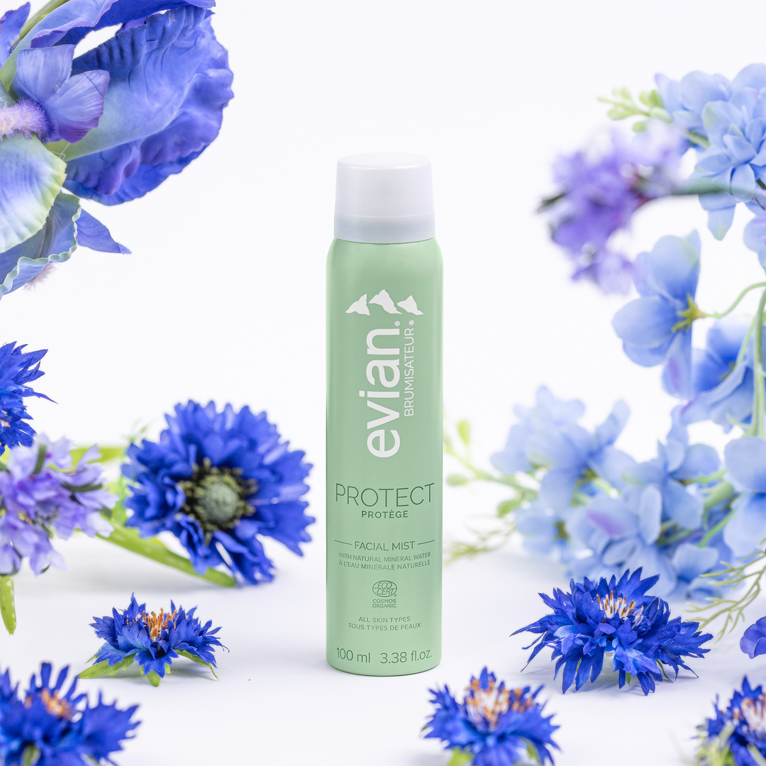 Evian facial mist bottle surrounded by blue flowers on a white background