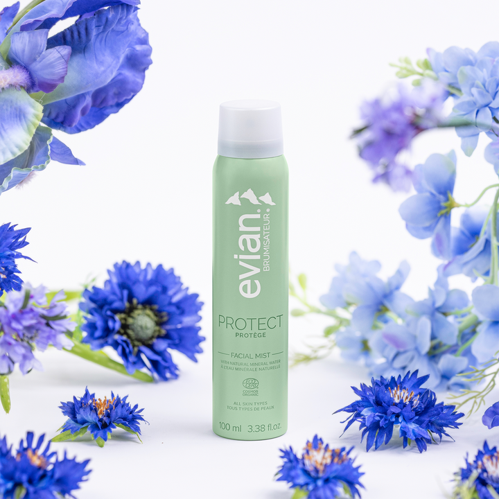 Evian facial mist bottle surrounded by blue flowers on a white background