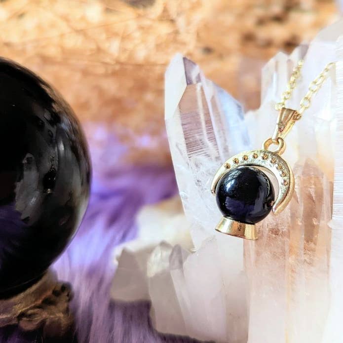 Crystal Ball Necklace hanging off of quartz next to a real obsidian crystal ball 