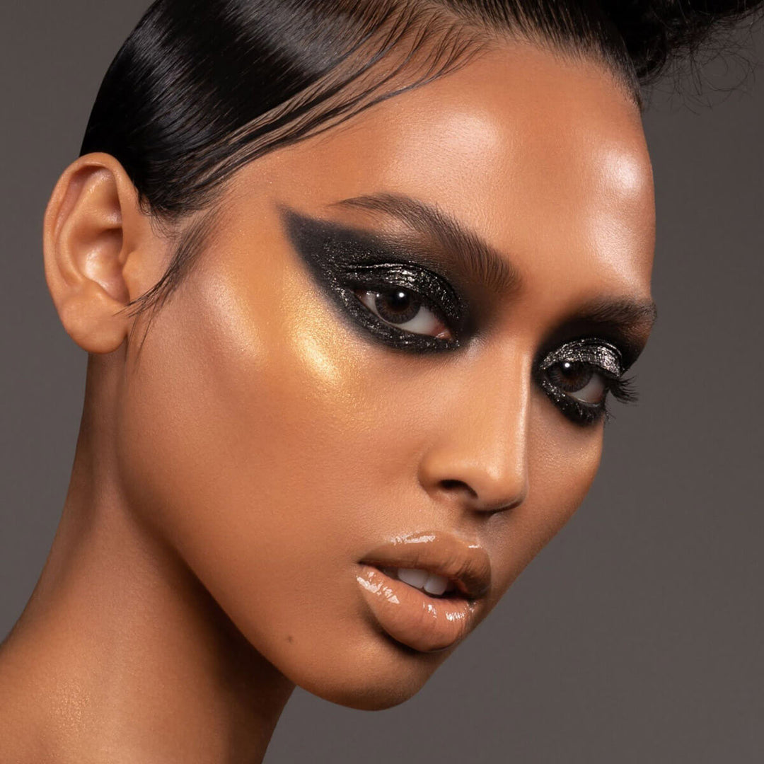 This is a model wearing the colorfix matte blackout shade on her eyes with a gold highlight and gold glitter on the eyes to accentuate the black eyes