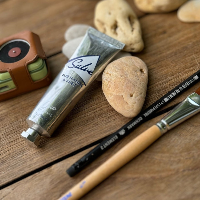 Tube of Salve, paintbrushes, and stones on a wooden surface